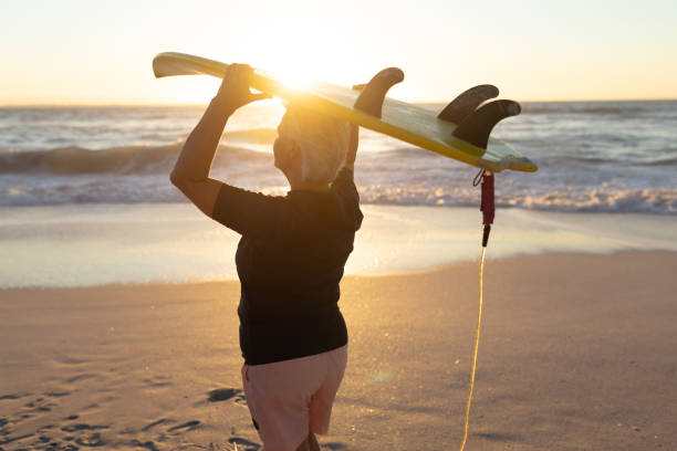 istock Old woman with a surfboard at the beach 1204628500