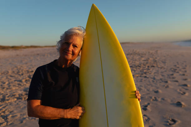 istock Old woman with a surfboard at the beach 1204628507