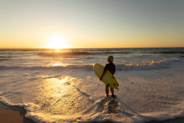 istock Old woman with a surfboard at the beach 1204628533