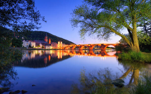 Heidelberg, the Old bridge at dusk Heidelberg, Germany, dreamy dusk colors over the Neckar river with the Old Town and Bridge, framed by trees and their reflections heidelberg germany stock pictures, royalty-free photos & images