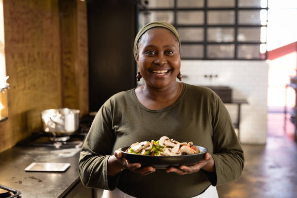 African woman showing her dish Front view of an Senior African woman at a cookery class, holding a bowl filled with vegetables. Active Seniors enjoying their retirement. serving dish stock pictures, royalty-free photos & images