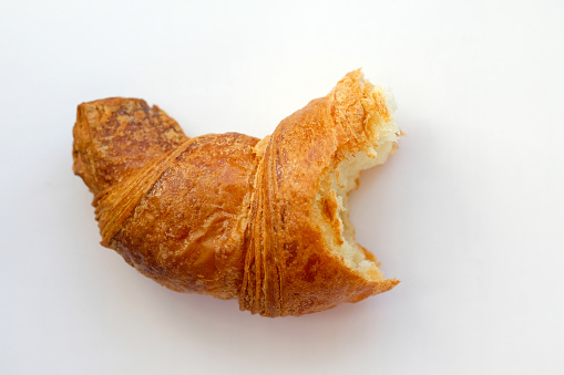 Bitten croissant on a white background. A slice of fresh croissant top view. French pastry with golden crust for breakfast. Diet rejection of baked pastry.