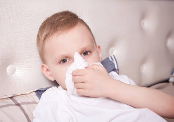istock Sick little blond boy blowing her nose 1204633175