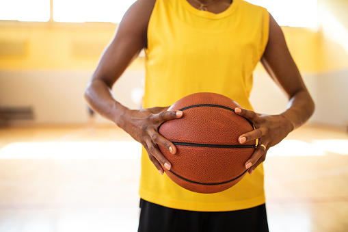 Unrecognizable black female basketball player holding basketball ball while standing on basketball court