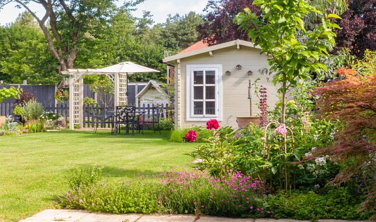English garden in summer with summerhouse with trees, plants and flowers.