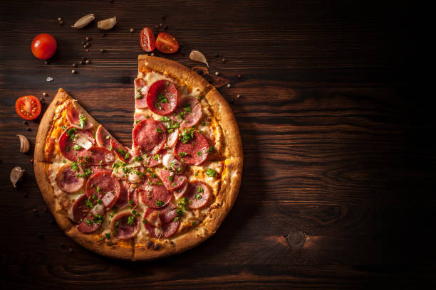 istock Pizza with salami, ham, bacon, garlic and fresh herbs. Rustic style. 1204634462