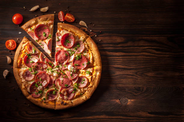 istock Pizza with salami, ham, bacon, garlic and fresh herbs. Rustic style. 1204634568