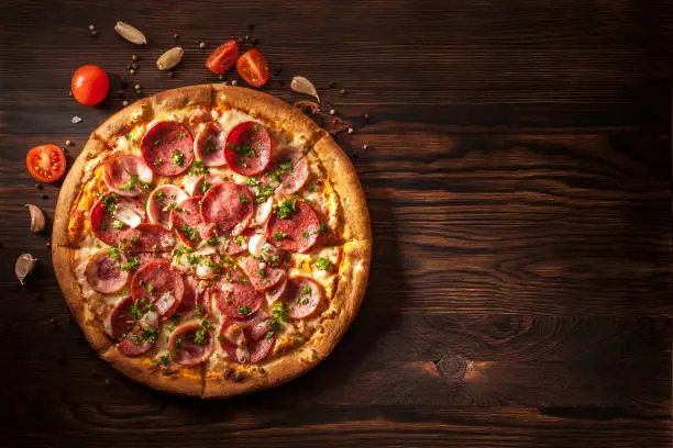 Pizza with salami, ham, bacon, garlic and fresh herbs. Rustic style. Top view. Copy space.