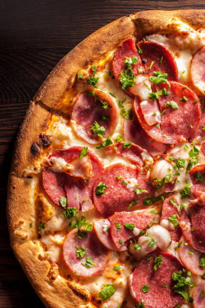 Pizza with salami, ham, bacon, garlic and fresh herbs. Rustic style. stock photo