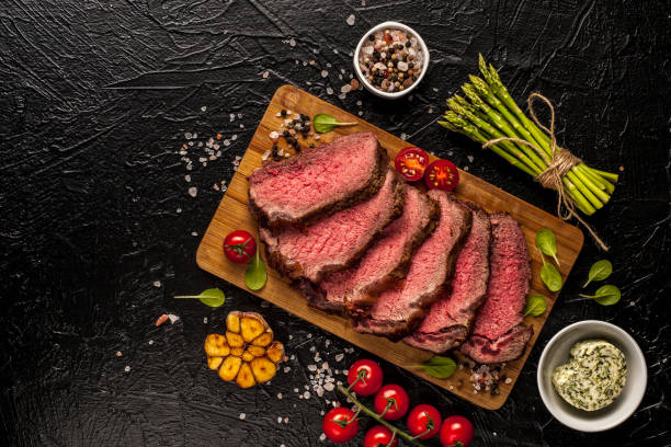 Roast beef. A large piece of meat with fresh vegetables is cut on a board and ready to eat. stock photo