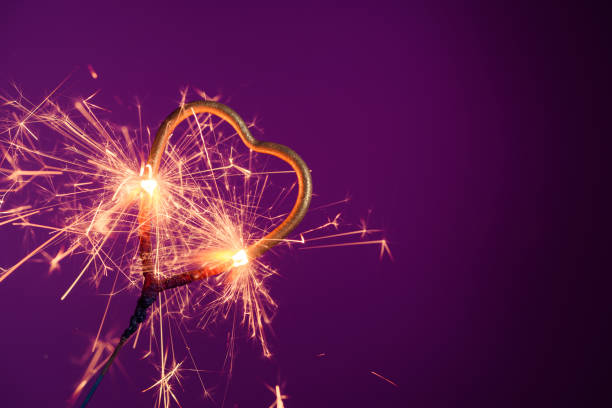 istock Sparkler in love heart shape on a purple background 1204637258