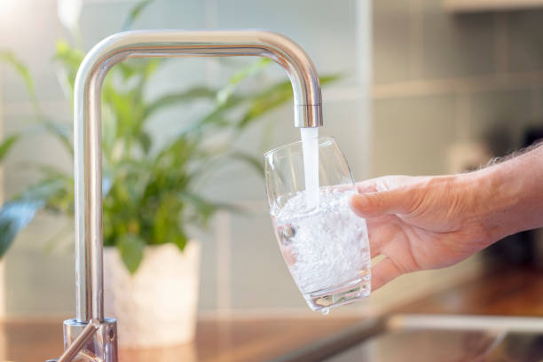 заполнение стакана питьевой водой из кухонного крана - faucet стоковые фото и изображения