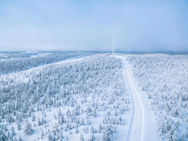 Photo of Aerial view of windmill in winter forest with snow road in Finland.