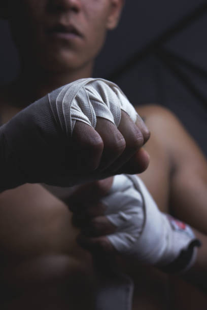 istock Male athlete, Muay Thai, wears a white hand tie to protect his hands while practicing. The concept of a martial athlete posing indoors 1204639602