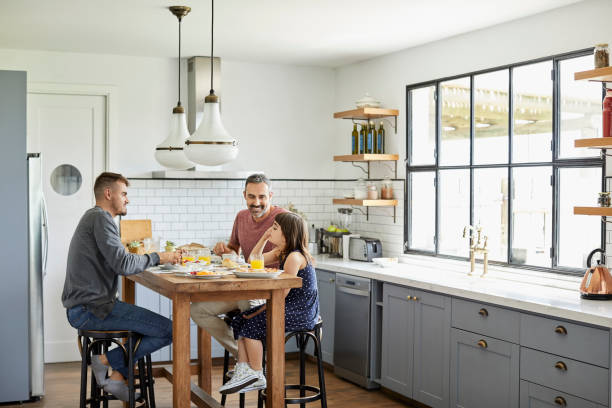 Family eating breakfast in kitchen at home Full length of family eating breakfast at table in kitchen. Homosexual fathers are sitting with daughter. They are in casuals at home. gay daddy stock pictures, royalty-free photos & images