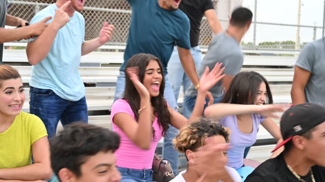 Hispanic male and female teenagers cheering from bleachers