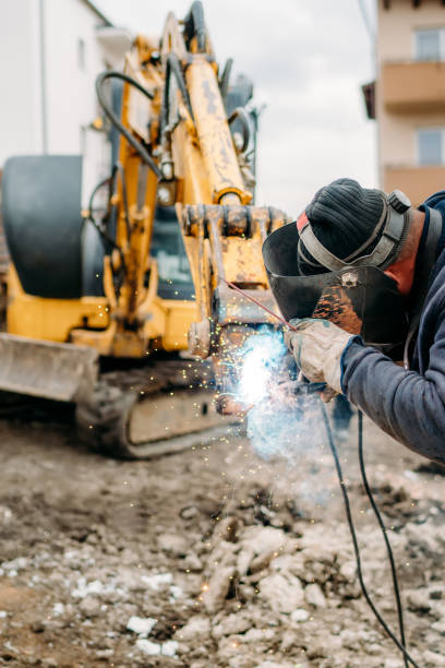 istock Professional welder with protection gear and mask welding broken excavator arm 1204643889