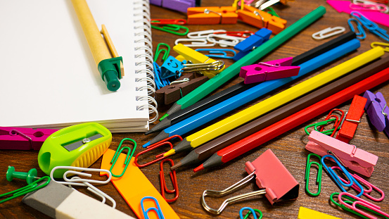 Multicolored Pencils, Paper Clips and Notebook. School stationery on brown wooden table. Back to school, education or knowledge