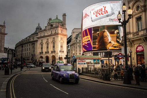 31st January, 2020 - London Cabs and Traffic driving around the famous Piccadilly Circus in London at dusk with its iconic building with advertisement panels illuminating the scene