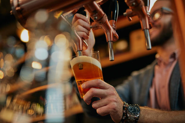 barman caucásico tatuado sirviendo cerveza mientras está de pie en el pub. - pint glass fotografías e imágenes de stock