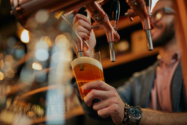 barman caucasico tatuato che versa birra mentre si trova al pub. - scodella foto e immagini stock