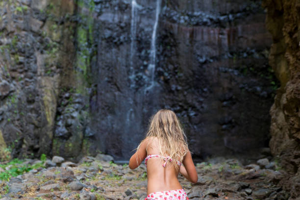 Young girl in bikini walking toward the waterfall at Madeira Island during summer holidays