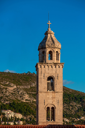 Medieval catholic church tower with bell cote, hills on background