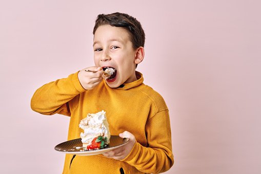 Cute child eating cake on pink background.