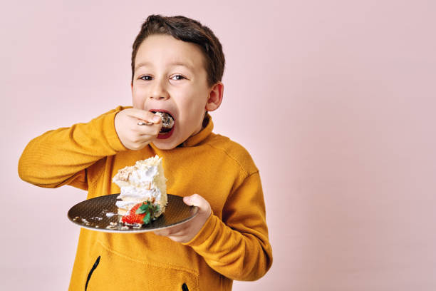 istock Cute child eating cake on pink background. 1204658819