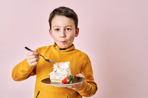 istock Cute child eating cake on pink background. 1204659007