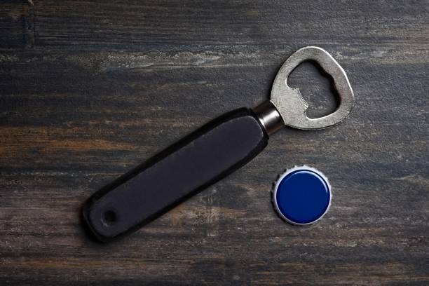 istock Bottle opener beside a bottle cap lying on a wooden table. High angle view with copy space. 1204660258