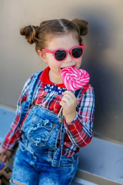 Girl with loly-pop on the street. Baby girl of 5 years on walk dressed in stylish denim