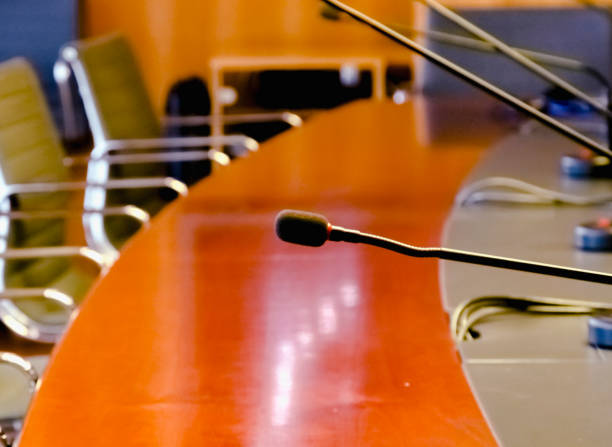 istock a table microphone in a board room with a wooden table and a row of empty chairs 1204666927