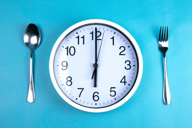 istock A clock showing exactly 6 hours, next to a fork and a spoon are on a blue background 1204672994