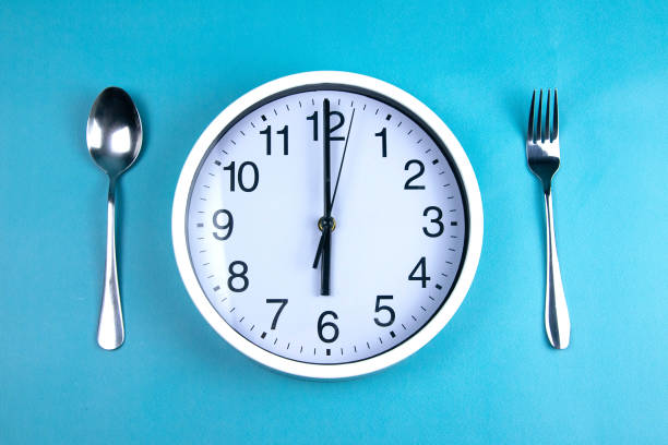 istock A clock showing exactly 6 hours, next to a fork and a spoon are on a blue background 1204672998