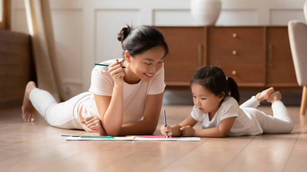 Young Vietnamese mom and little daughter painting at home Happy young Asian mother and cute little biracial daughter lying on warm wooden floor in living room painting together, millennial ethnic mom or nanny relax with small Vietnamese girl child drawing hot vietnamese women pictures stock pictures, royalty-free photos & images