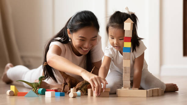 Overjoyed Vietnamese mother little daughter play at home Overjoyed young Asian mom and little biracial daughter lie on warm home floor construct with building bricks together, happy millennial Vietnamese mother have fun play with small girl child preschool student stock pictures, royalty-free photos & images