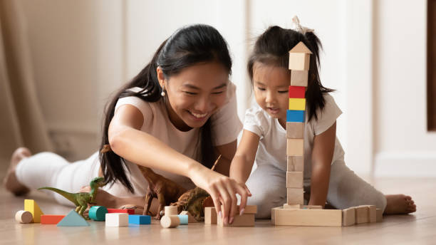 Overjoyed Vietnamese mother little daughter play at home Overjoyed young Asian mom and little biracial daughter lie on warm home floor construct with building bricks together, happy millennial Vietnamese mother have fun play with small girl child asian nanny stock pictures, royalty-free photos & images