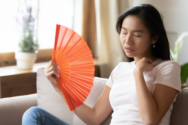Unhealthy young Asian woman breathe fresh air from waver Unwell young Asian woman sit on couch wave with hand fan feel sick at home, overheated millennial Vietnamese girl relax on sofa in living room breathe fresh air from waver, suffer from heatstroke hot vietnamese women pictures stock pictures, royalty-free photos & images