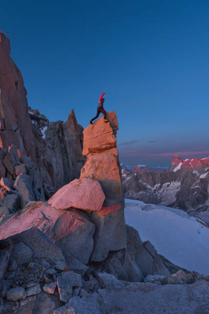 Man with hand raised up standing on a rock spire