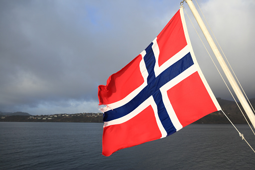 Norwegian Flag over Norwegian fjords background. Shallow DOF, Copy space on left