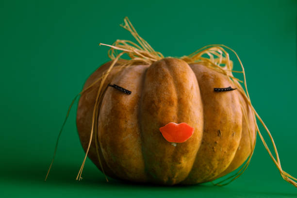 Pumpkin with eyelashes and mouth on green background.