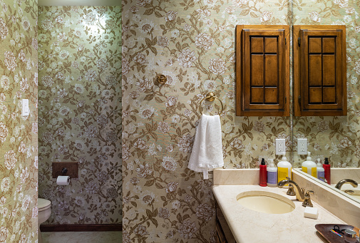 Interior of 1970's style master bathroom. Part of the family home in San Antonio, Texas. Design of the bathroom is original condition from the time it was made in mid 70s. Old fashioned wall paper design, old bathroom finishes and carpet in closet area. Gold trimmed faucet, pink marble bathtub.