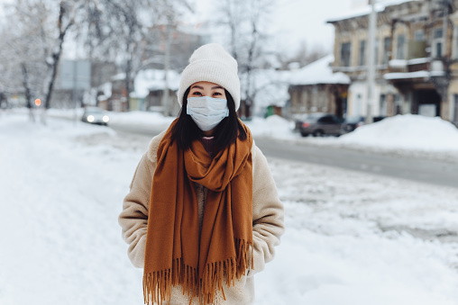 Passerby Asian girl in a protective medical mask outdoors. A woman on the street in winter protects the respiratory tract from the epidemic of coronavirus. Protection against urban smog and dust