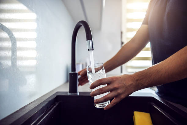 fermez-vous vers le haut de jeune homme versant l’eau fraîche de l’évier de cuisine. intérieur de la maison. - lavabo et évier photos et images de collection