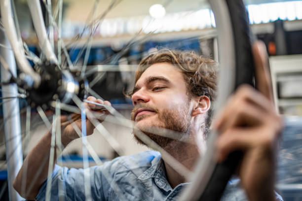 istock Young mechanic repairing bicycle wheel in workshop. 1204684018