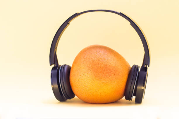 ripe bright grapefruit enjoys music in headphones on a yellow background. concept of fruit freshness and musical cocktail