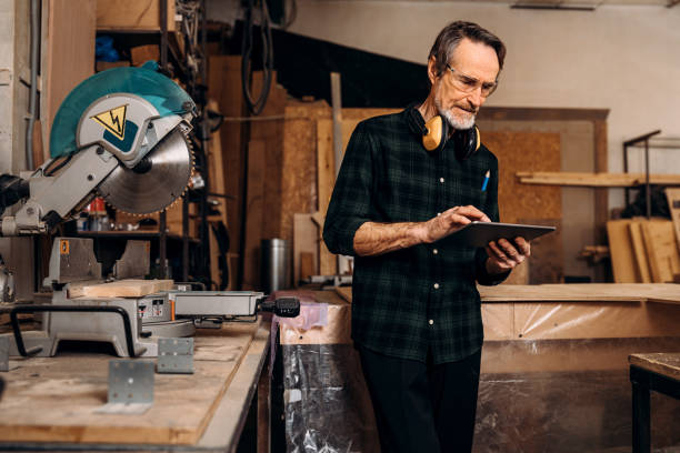 istock Mature carpenter holds a digital tablet. Male worker standing at workbench in carpentry. 1204689019