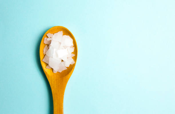 istock Magnesium Chloride Flakes scattered around brown wooden spoon on blue background. For making foot bath, taking a magnesium-rich bath allows full body exposure to a concentrated solution of magnesium. 1204692044