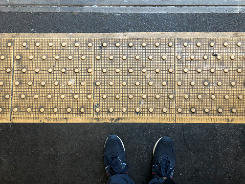Waiting on the platform of a London underground. PoV, looking down at dividing line, floor and shoes